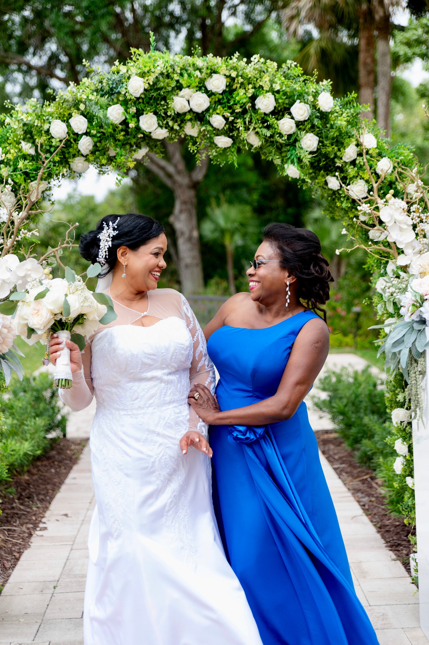 A bride in a white strapless wedding gown, design by Alexas and her mother in a bright blue one-shoulder gown