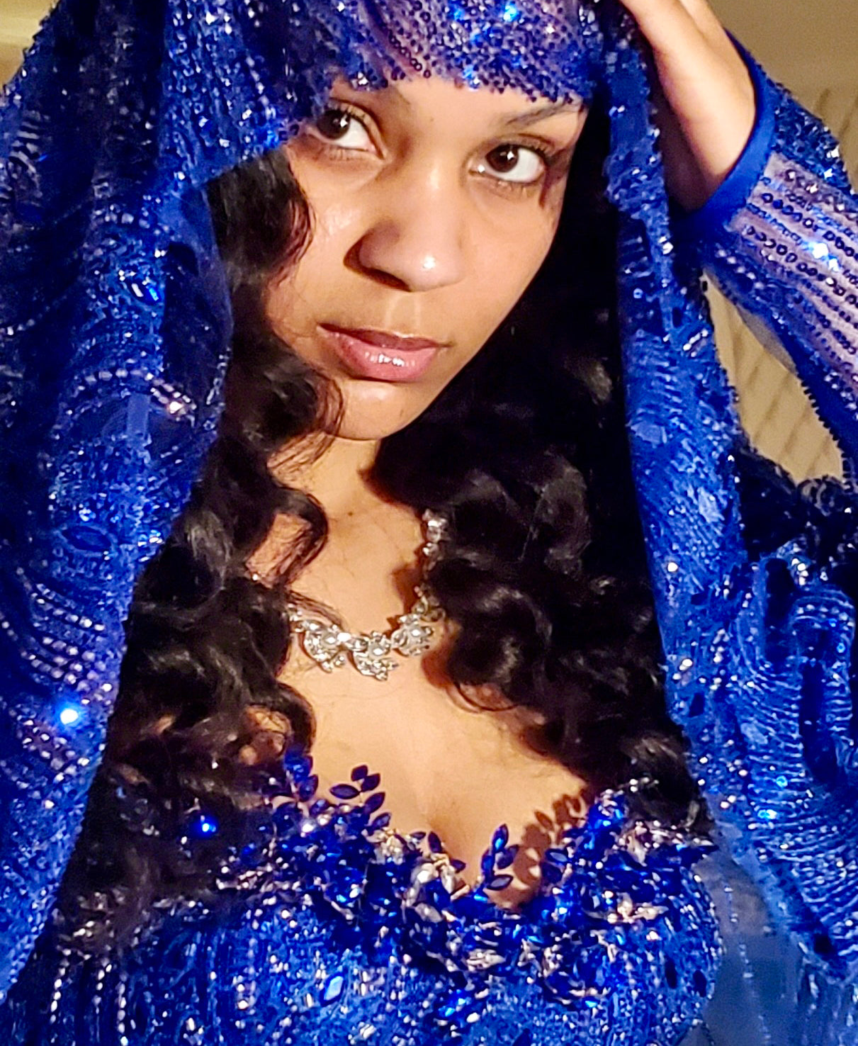 A woman wearing a sparkling royal blue beaded veil and matching embellished top, with a silver jeweled necklace, design by Alexas