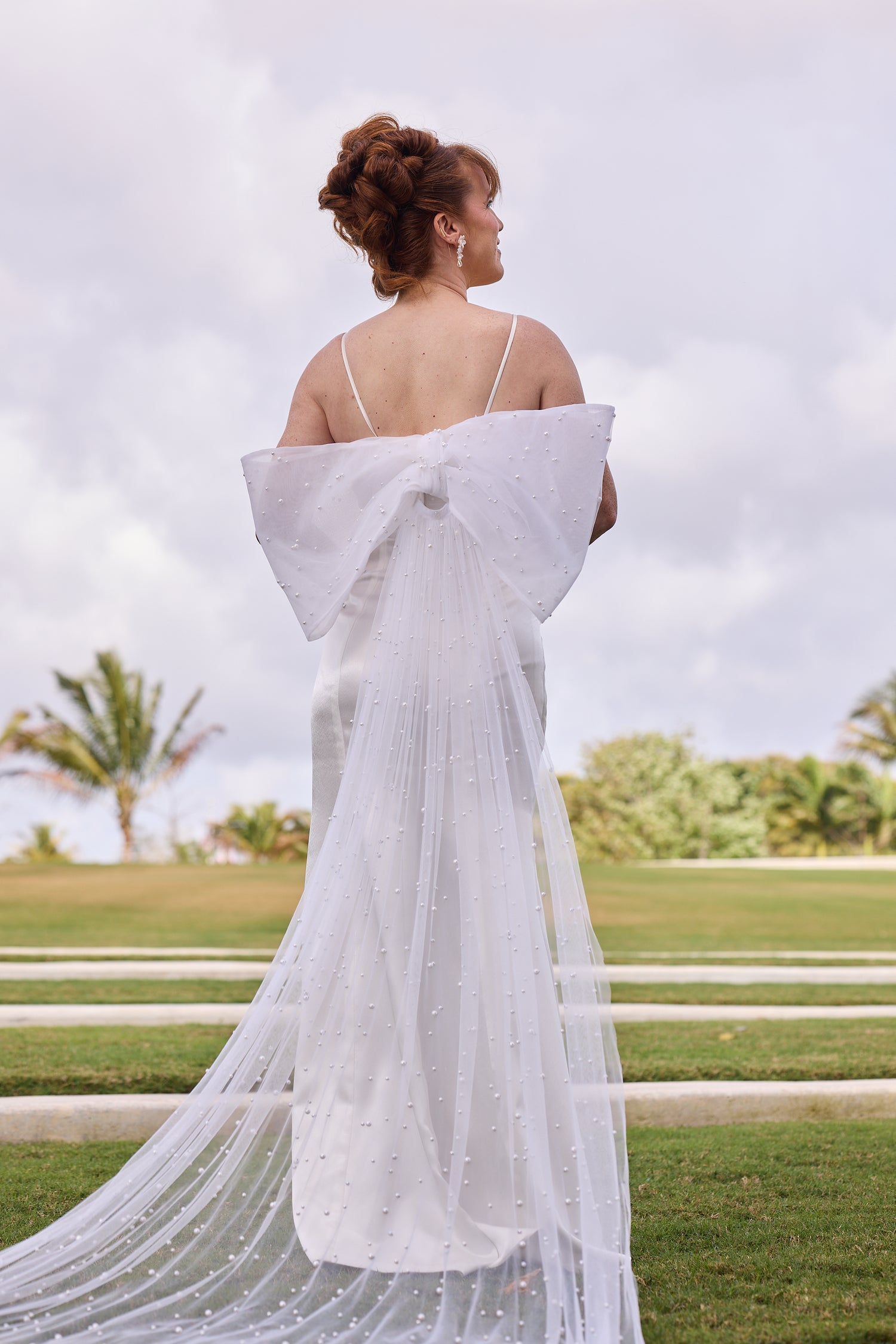 Woman in a white dress with a long train standing, design by Alexas