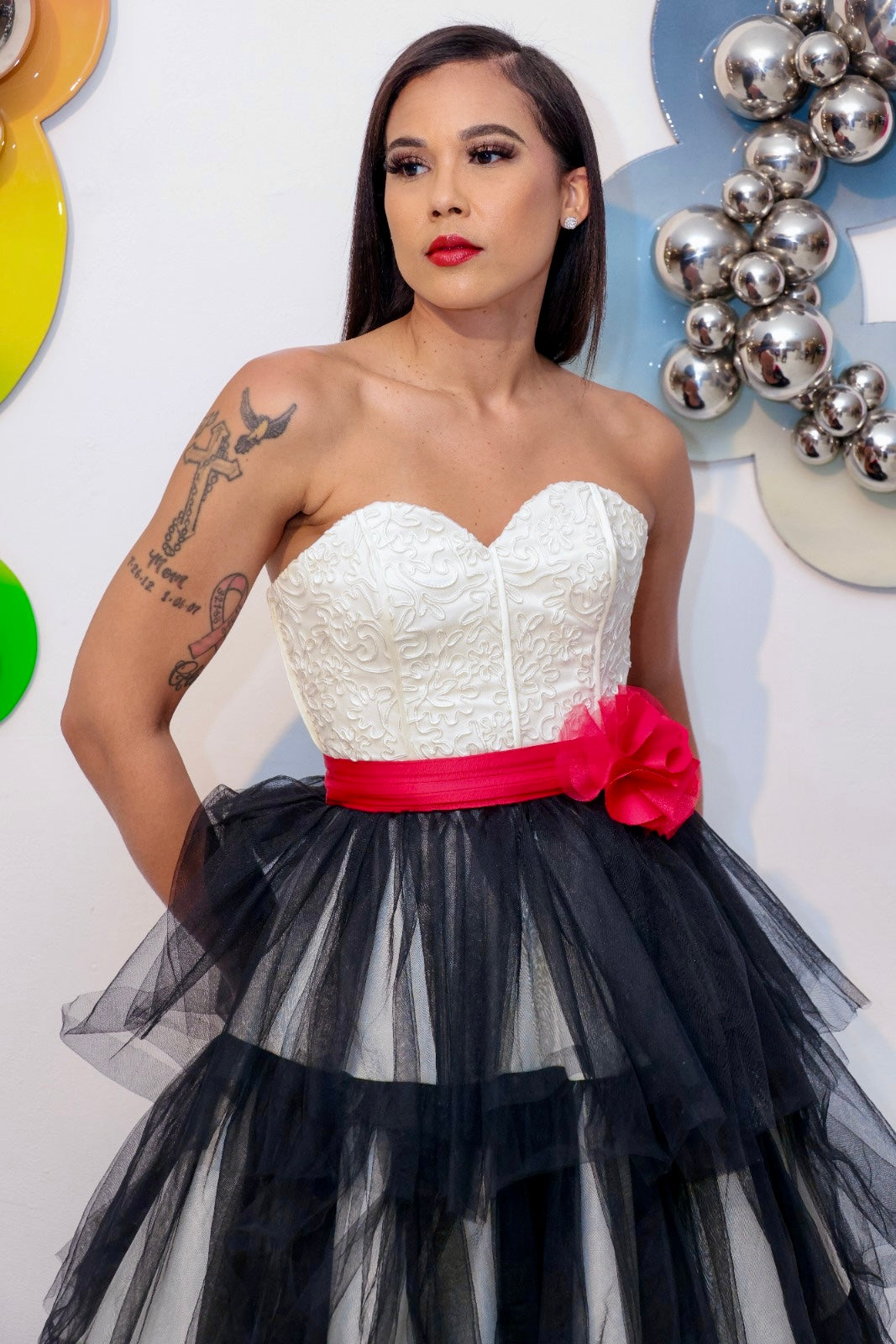 Woman wearing a strapless white top with a black tulle skirt and red bow, design by Alexas